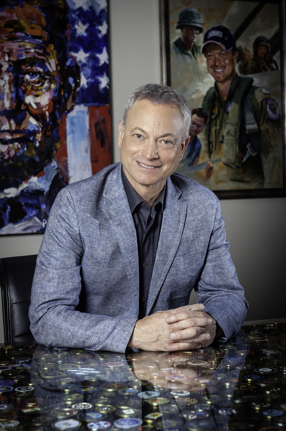 Gary Sinise in grey suit sitting at desk.