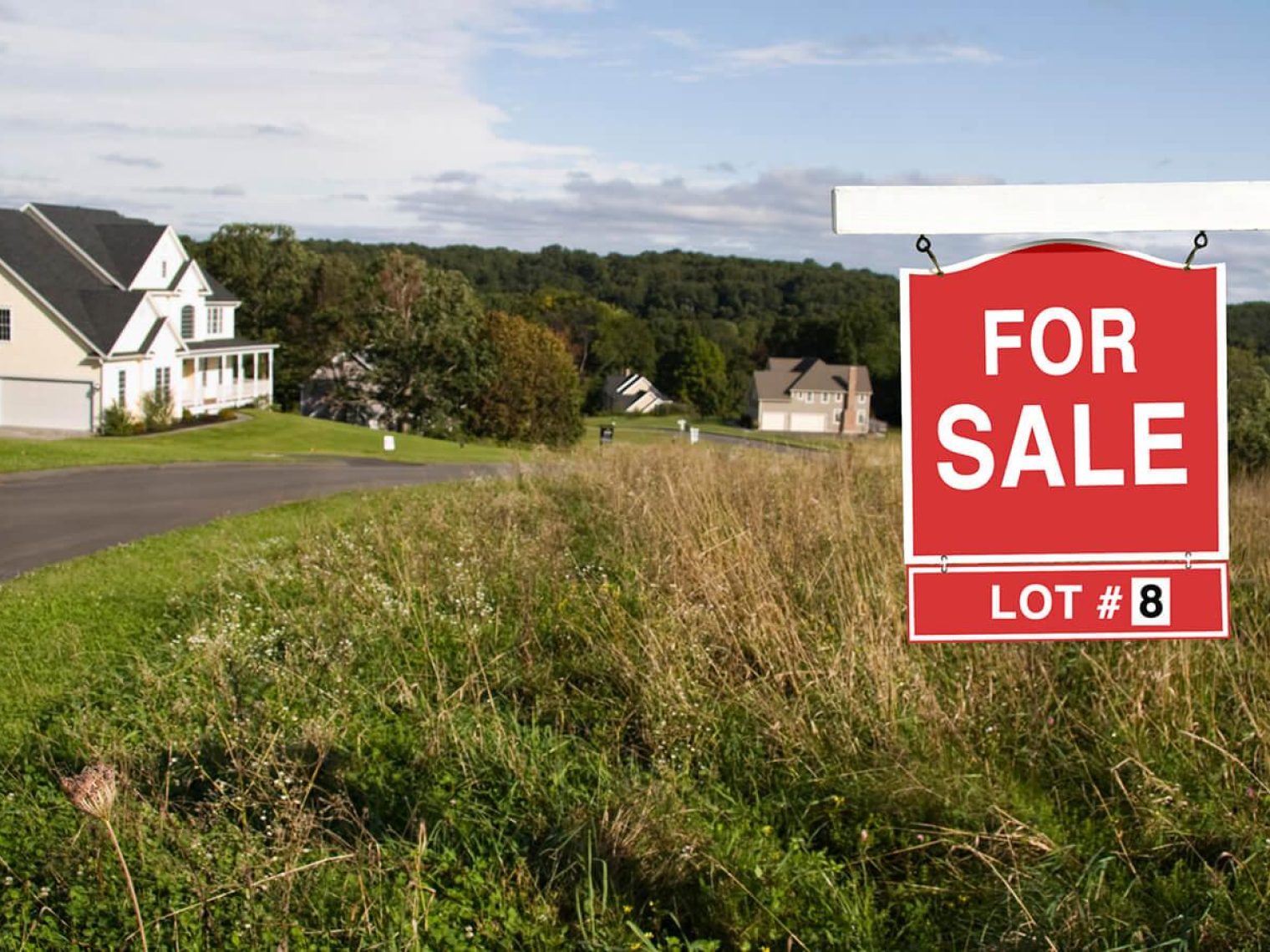 Red and white for sale sign in front of a large plot of land.