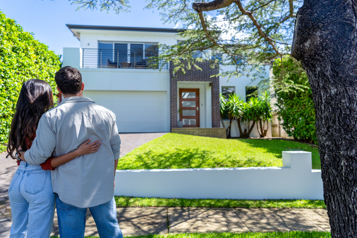 The back of a young couple standing in front of a home.