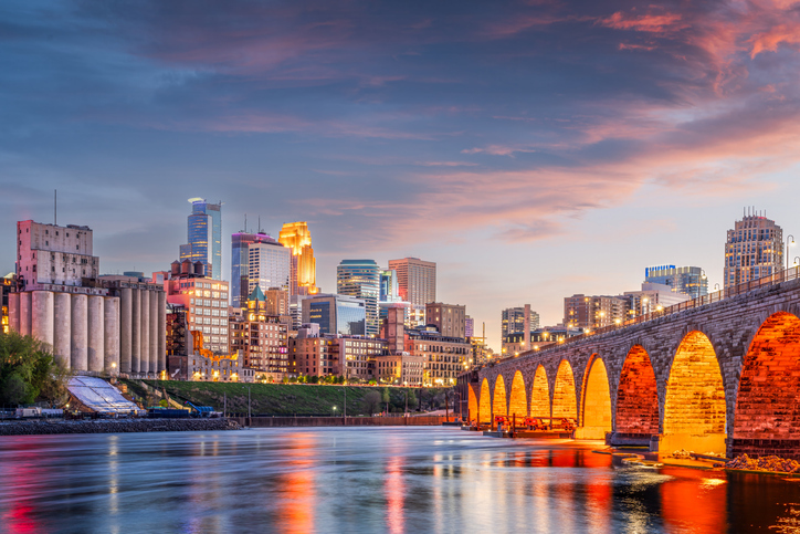 An image of part of the Minneapolis skyline from the side, with a view of a lit up bridge