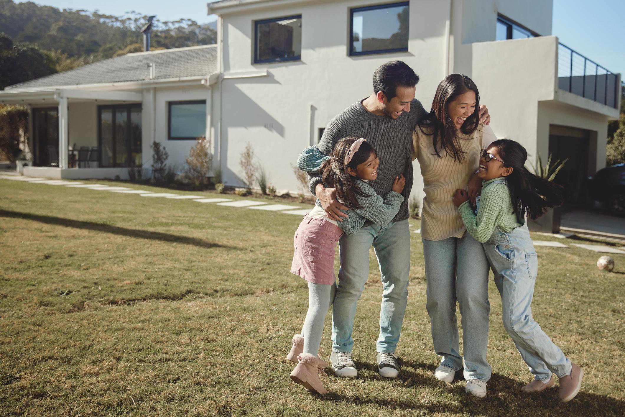 A family of four smiling and enjoying time outside their home.