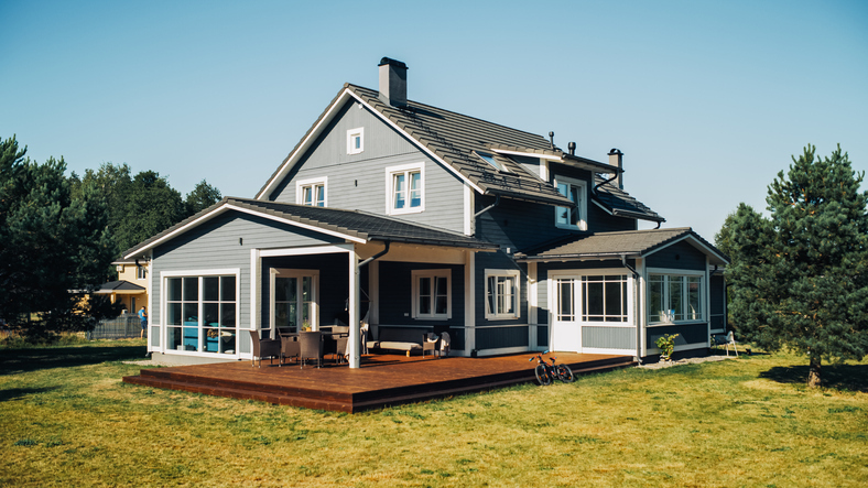 A charming two-story house with a spacious wooden deck and lawn, showcased on a sunny day.